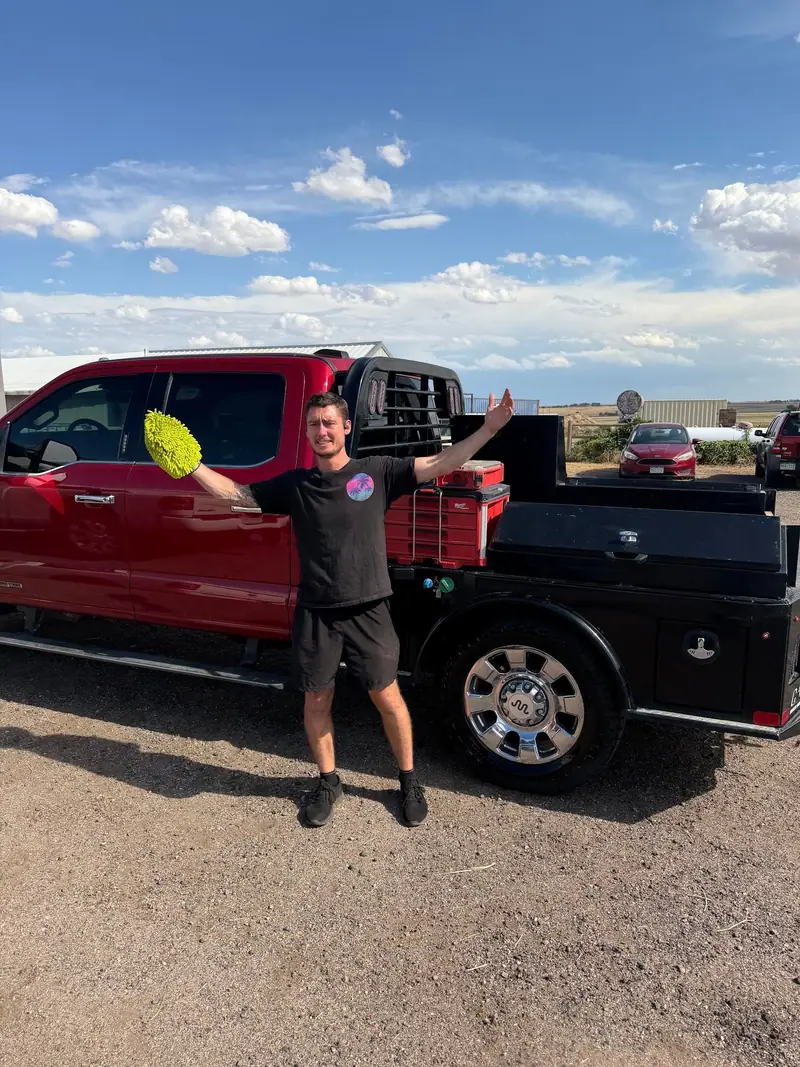 KJ of KJ Auto Detail with a wash mitt beside a freshly detailed red Ram flatbed on the plains