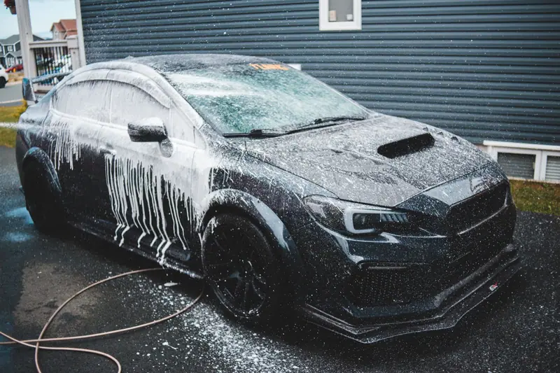 Dark car covered in wash foam in a home driveway